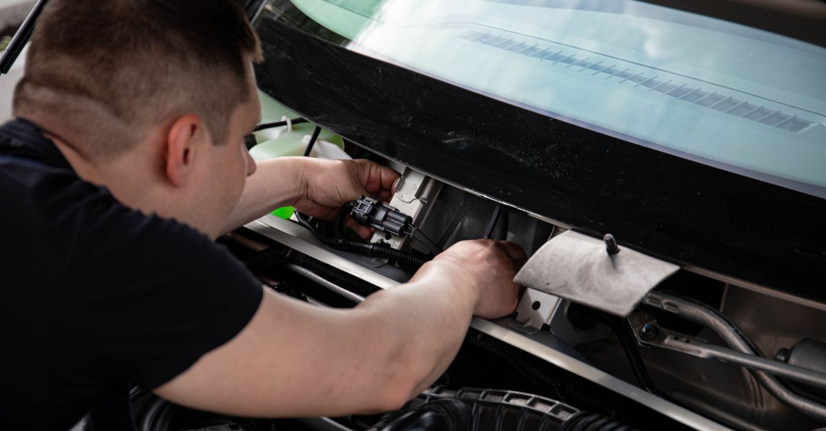 A mechanic working on car engine repairs inside a workshop setting.